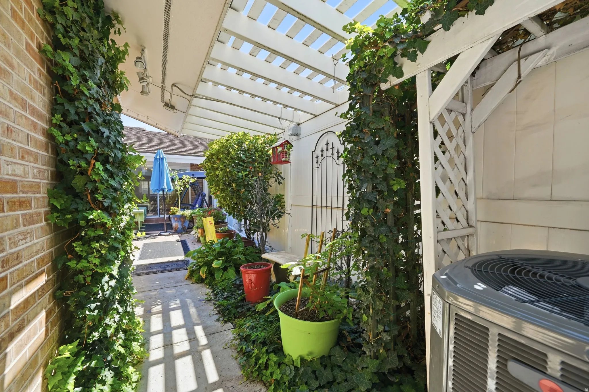 Pergola-covered walkway with brick siding, lattice accents, and established plantings