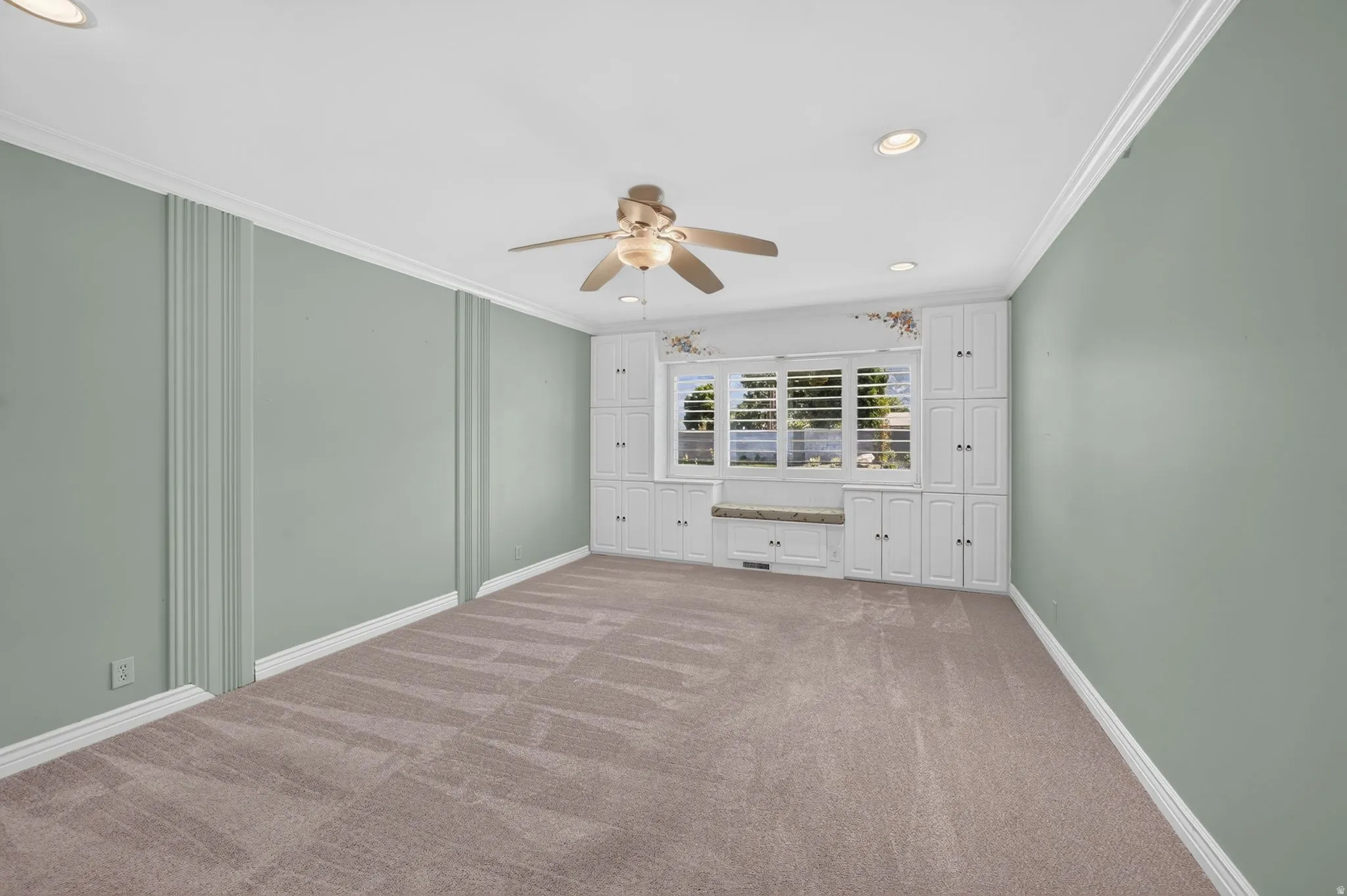 Built-in cabinetry with window seating, plantation shutters, crown molding, recessed lighting, and a ceiling fan
