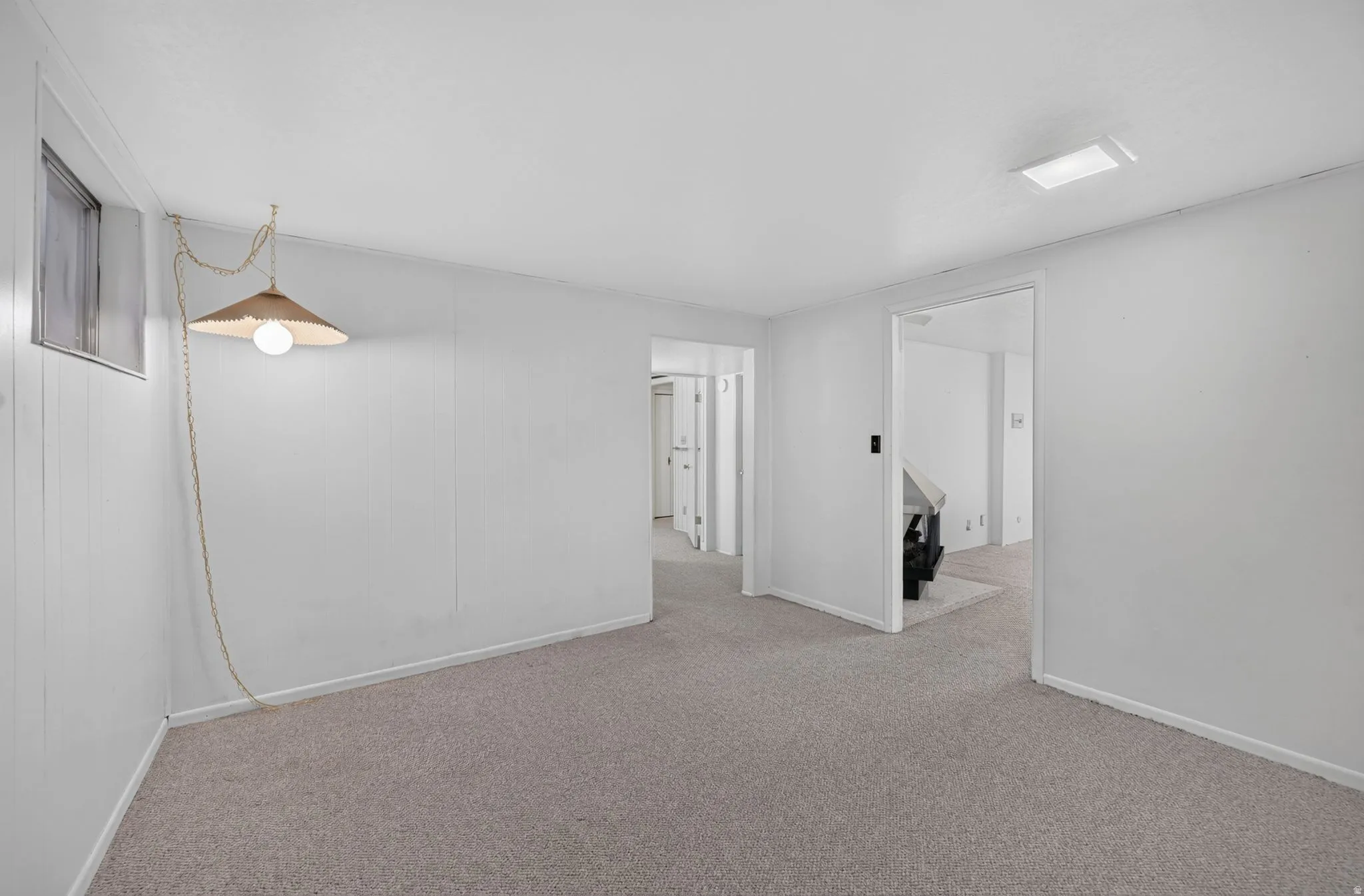 Carpeted flooring, white wall paneling, ceiling-mounted lighting, and a window