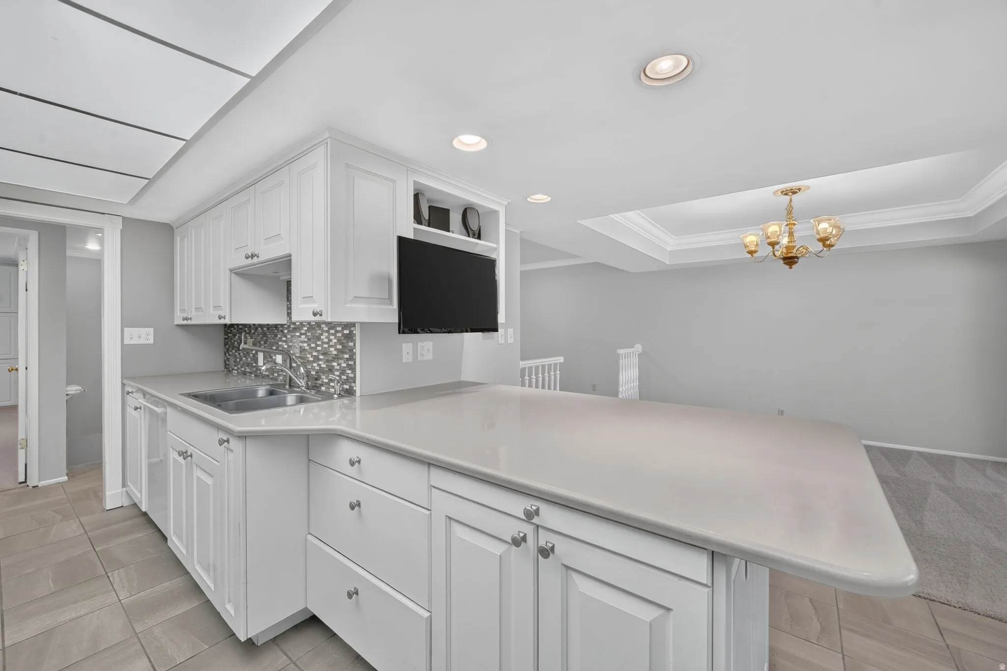 White cabinetry with brushed nickel hardware, gray tile flooring, stainless steel double-basin sink, mosaic tile backsplash, and light-toned countertops