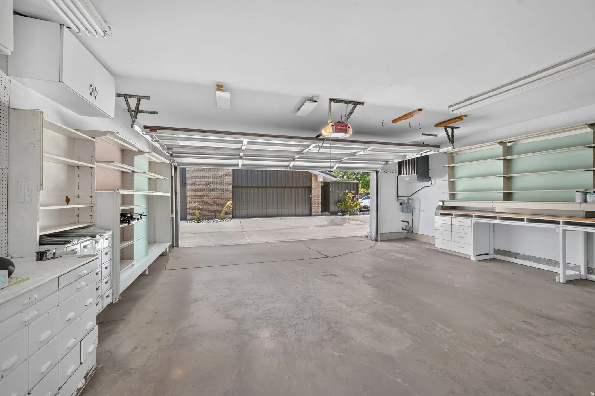 Attached two-car garage featuring a concrete floor, built-in shelving, white cabinetry, and a workbench