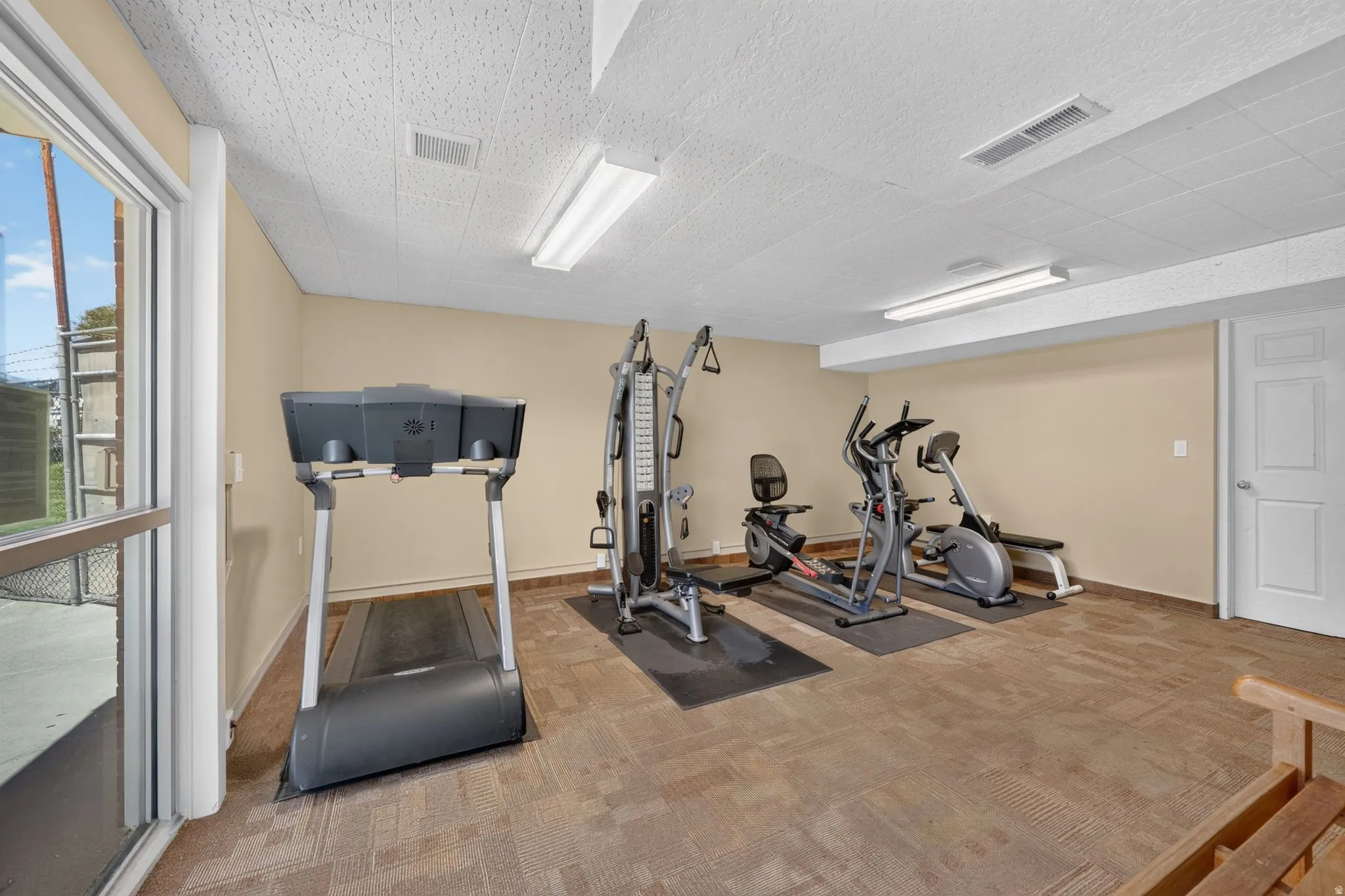 Fitness area with carpet tile flooring, light neutral wall paint, and white paneled door