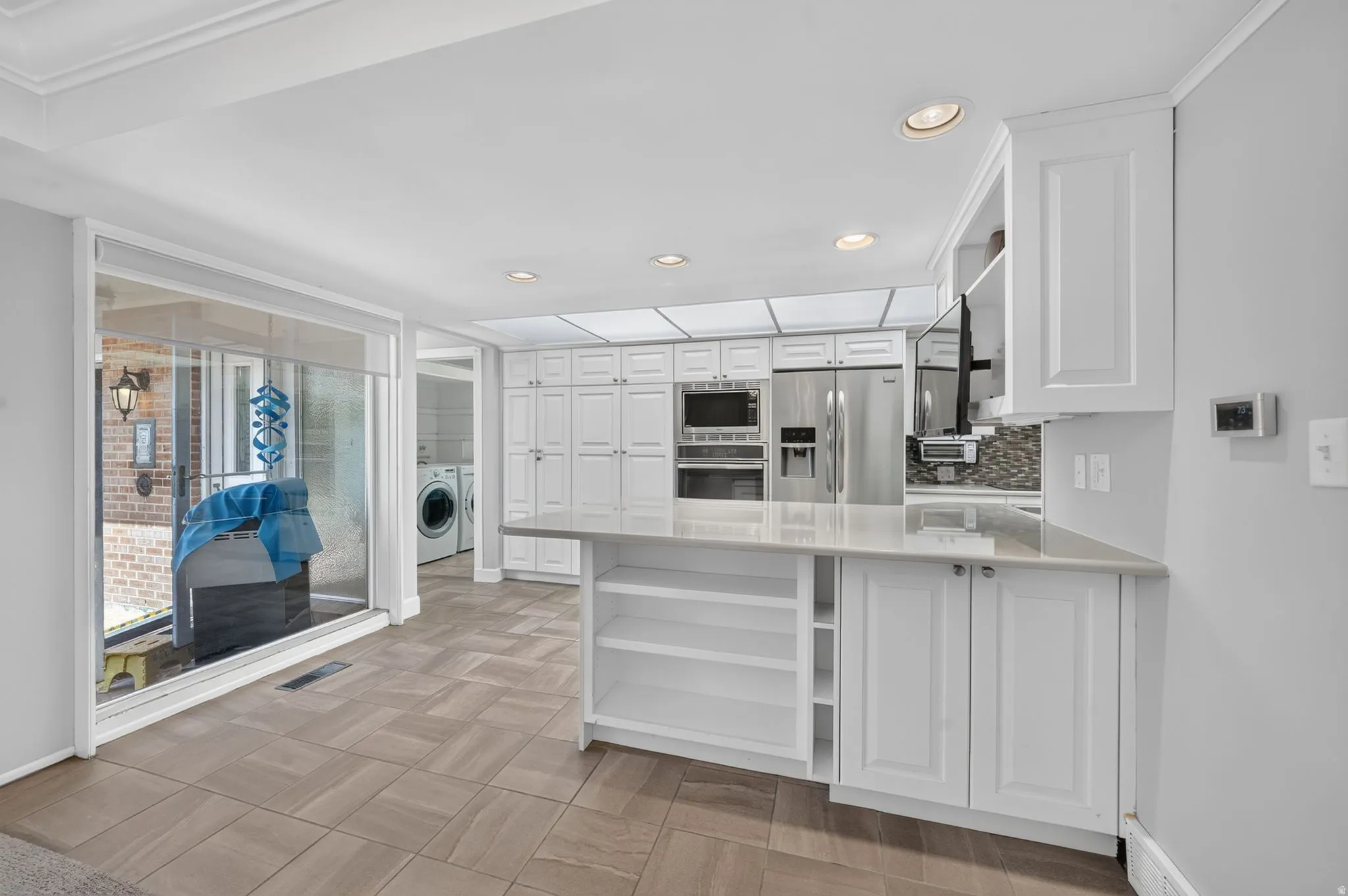 White cabinetry with integrated stainless steel appliances, stone countertops, and tile flooring