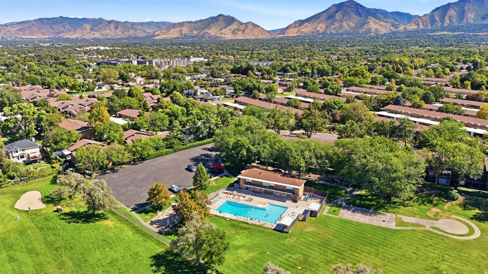 Expansive outdoor swimming pool, adjacent building, surrounded by green lawns and mature trees, with distant mountains