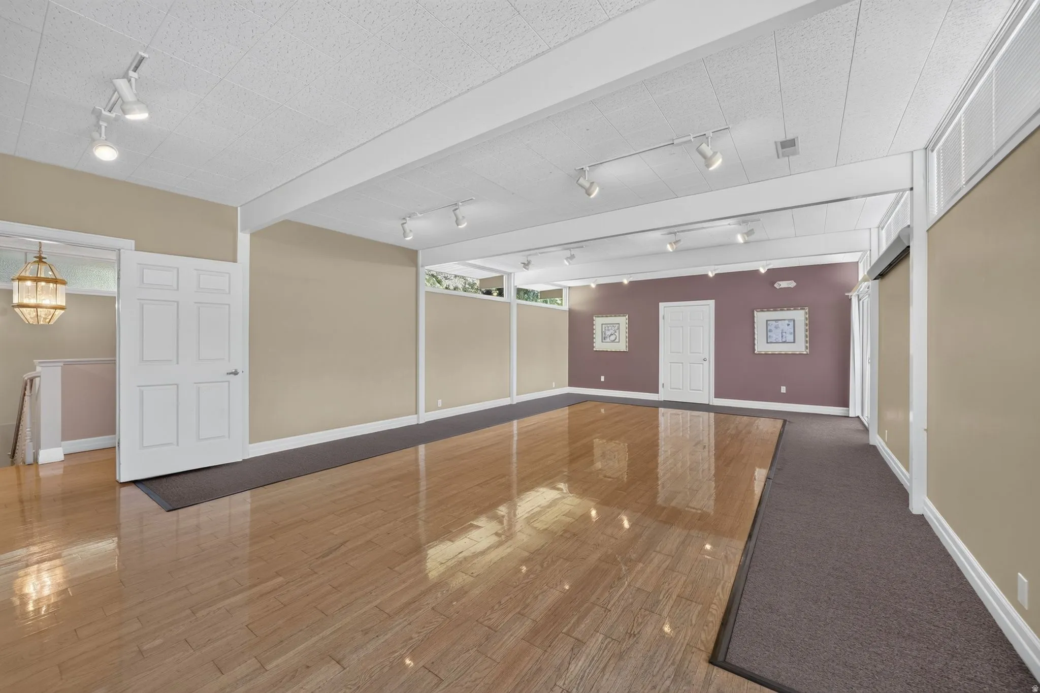 Expansive room featuring glossy wood-finish flooring, track lighting, and a textured drop ceiling
