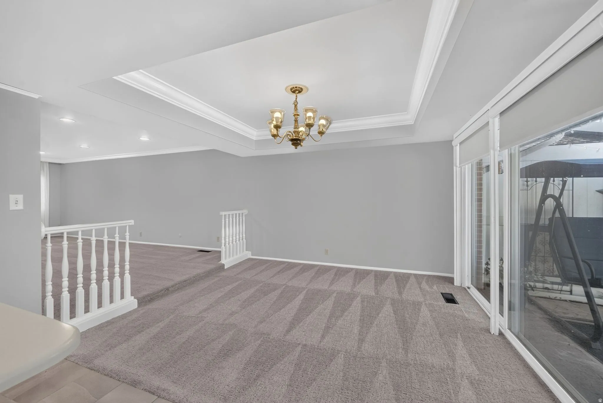 Recessed ceiling with decorative trim, brass chandelier, light gray wall finish, patterned carpeting, and white railing