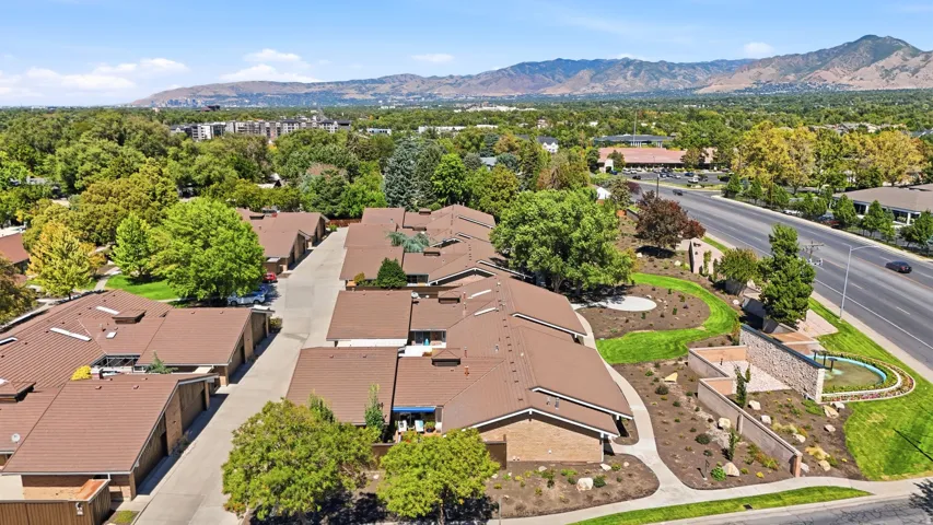 Expansive mountain backdrop, community landscaping, mature trees, brown shingle roofs, and a multi-lane road