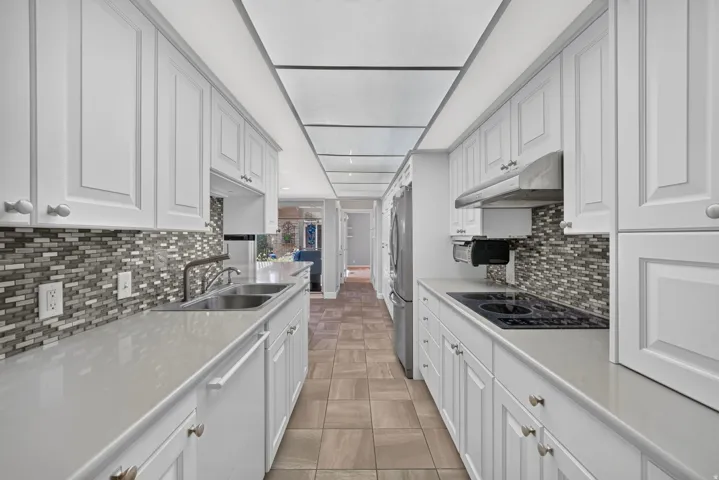 Galley kitchen featuring white cabinetry, light countertops, mosaic tile backsplash, stainless steel appliances, and tile flooring