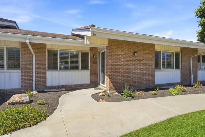 Brick exterior with white trim and white paneling, featuring a concrete walkway, landscaped garden beds, and a covered entry