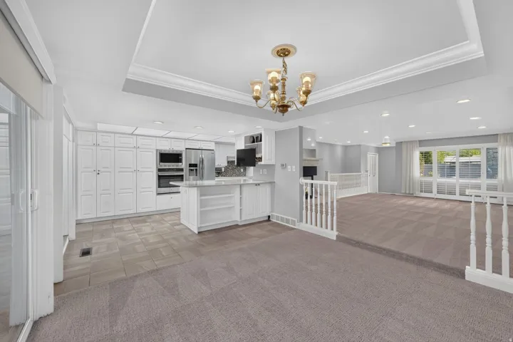 Recessed lighting, large white cabinetry, stainless steel appliances, central island with seating, and a decorative chandelier