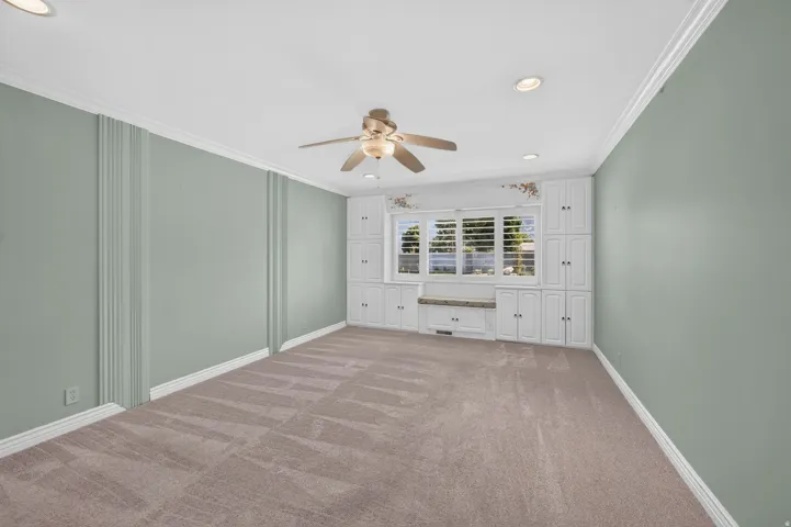 Built-in cabinetry with window seating, plantation shutters, crown molding, recessed lighting, and a ceiling fan
