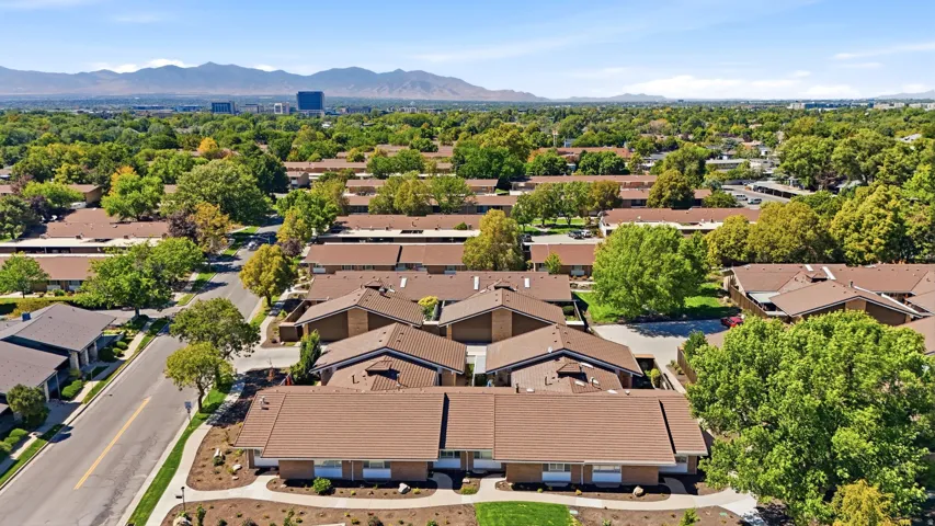 Aerial perspective showcasing multiple residential buildings with brown roofs, mature trees, landscaped grounds, and a paved street