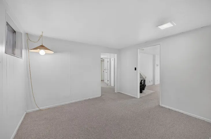 Carpeted flooring, white wall paneling, ceiling-mounted lighting, and a window