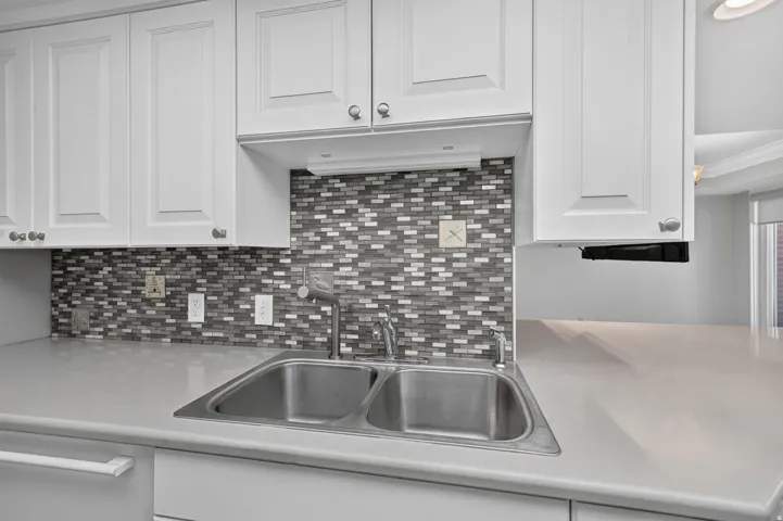 White cabinetry with silver-tone hardware, mosaic tile backsplash, double basin stainless steel sink, and light-toned countertop