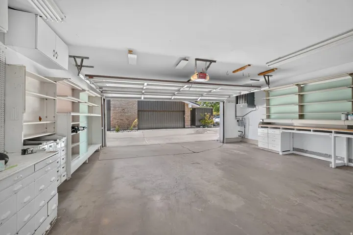Attached two-car garage featuring a concrete floor, built-in shelving, white cabinetry, and a workbench