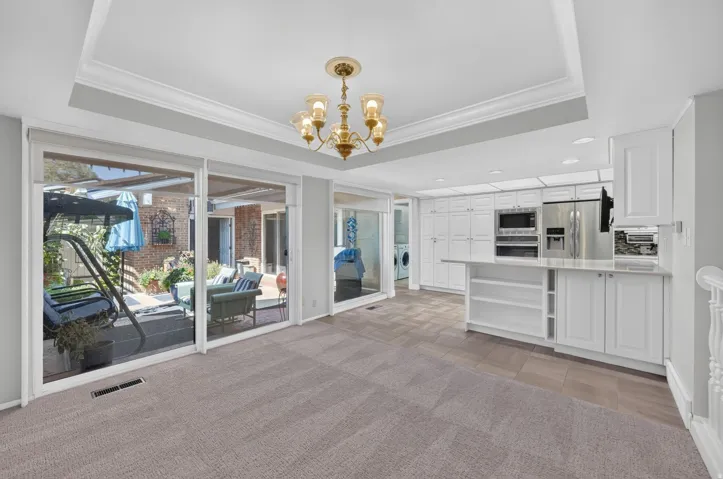 Tray ceiling with crown molding, brass chandelier, sliding glass doors, white cabinetry, and stainless steel appliances