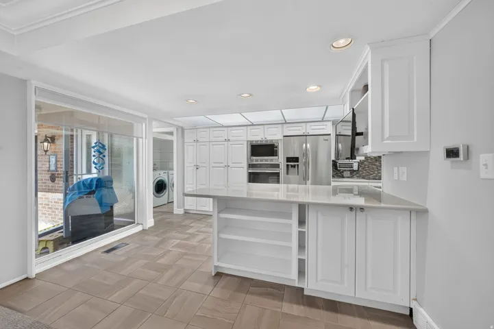 White cabinetry with integrated stainless steel appliances, stone countertops, and tile flooring