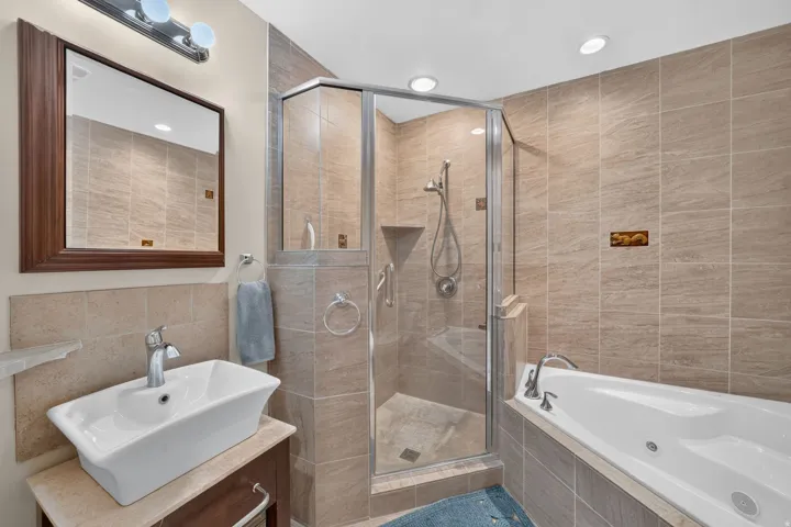 Tiled bathroom featuring a glass-enclosed shower, built-in bathtub, vessel sink, and recessed lighting