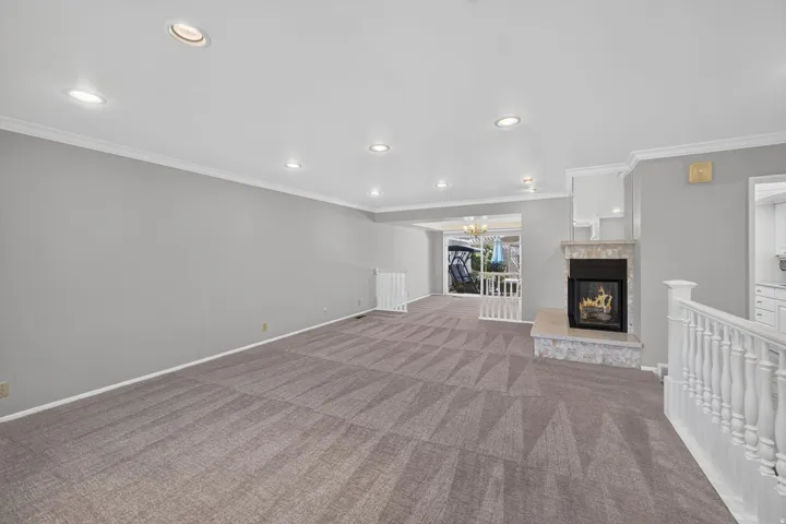 Recessed lighting, crown molding, and neutral wall tones complement the patterned carpeting