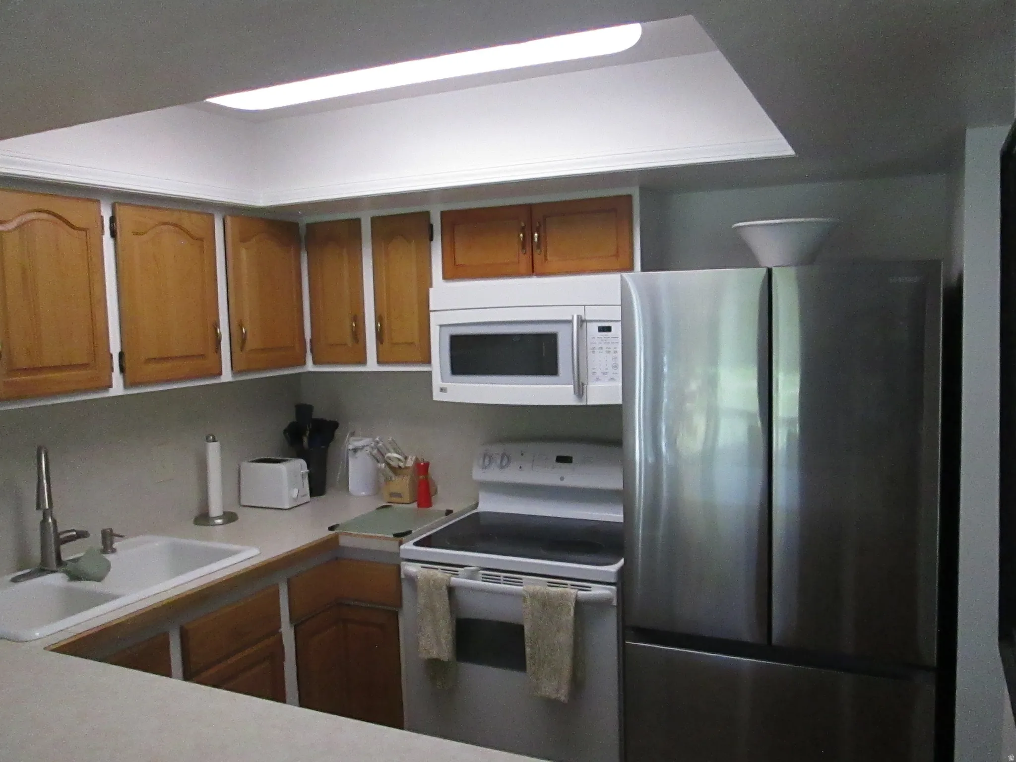 Kitchen featuring wood-finish cabinetry, white countertop, stainless steel refrigerator, white electric range, and a built-in microwave