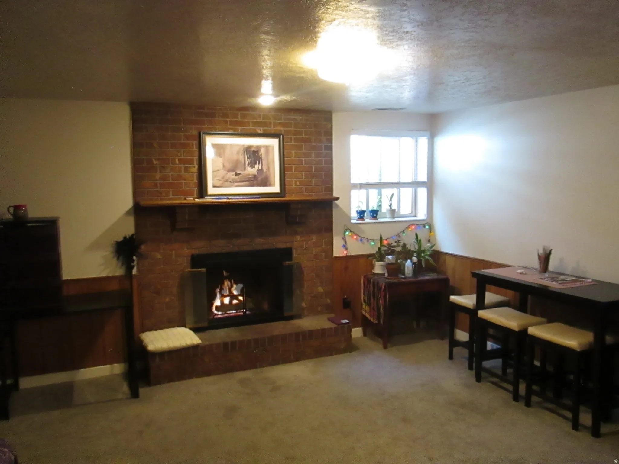 Brick-faced fireplace with a wood mantel, wainscoting, and carpet flooring