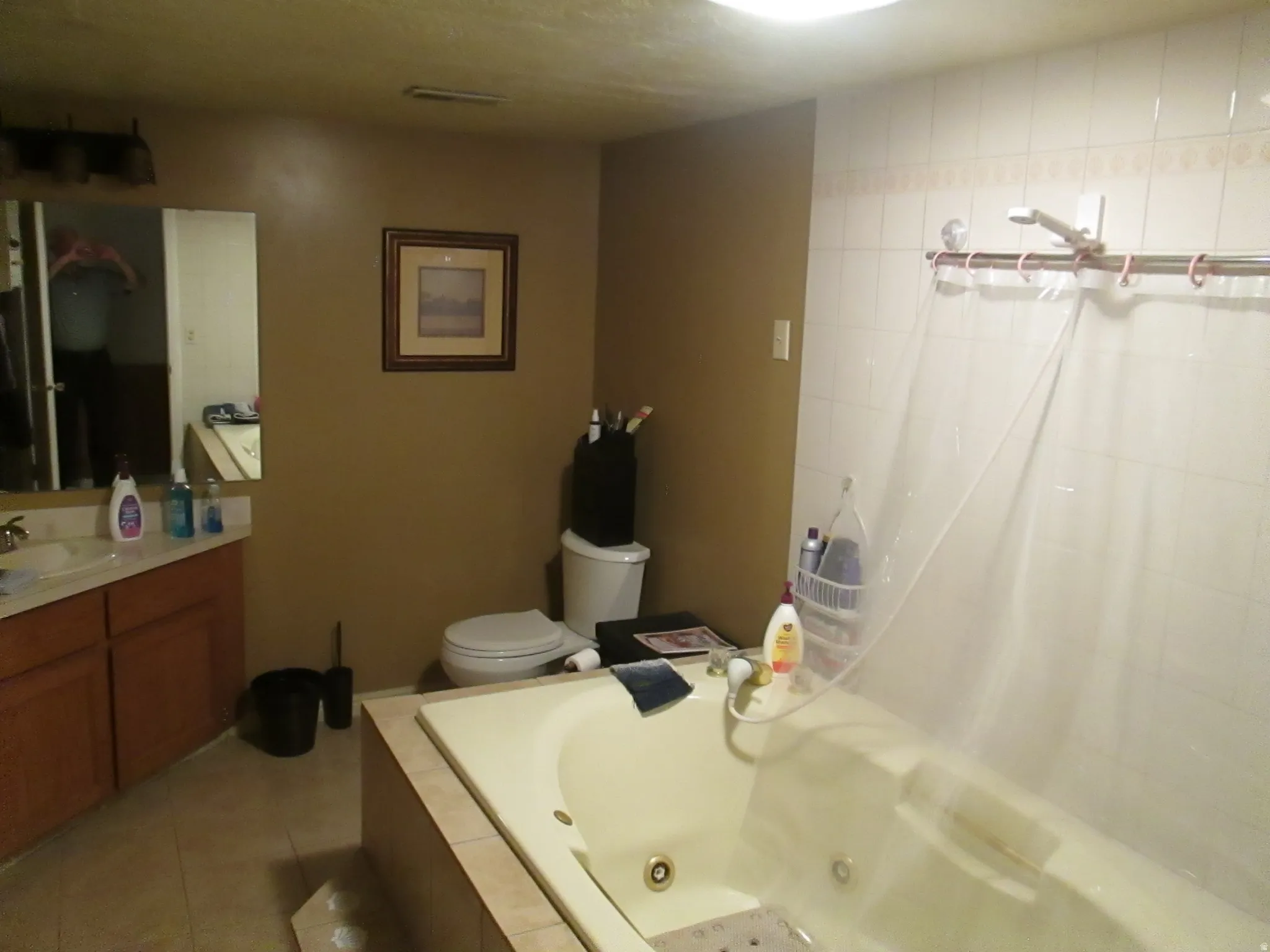 Built-in soaking tub with surrounding tile, single vanity with wood-finish cabinetry, and tiled shower walls