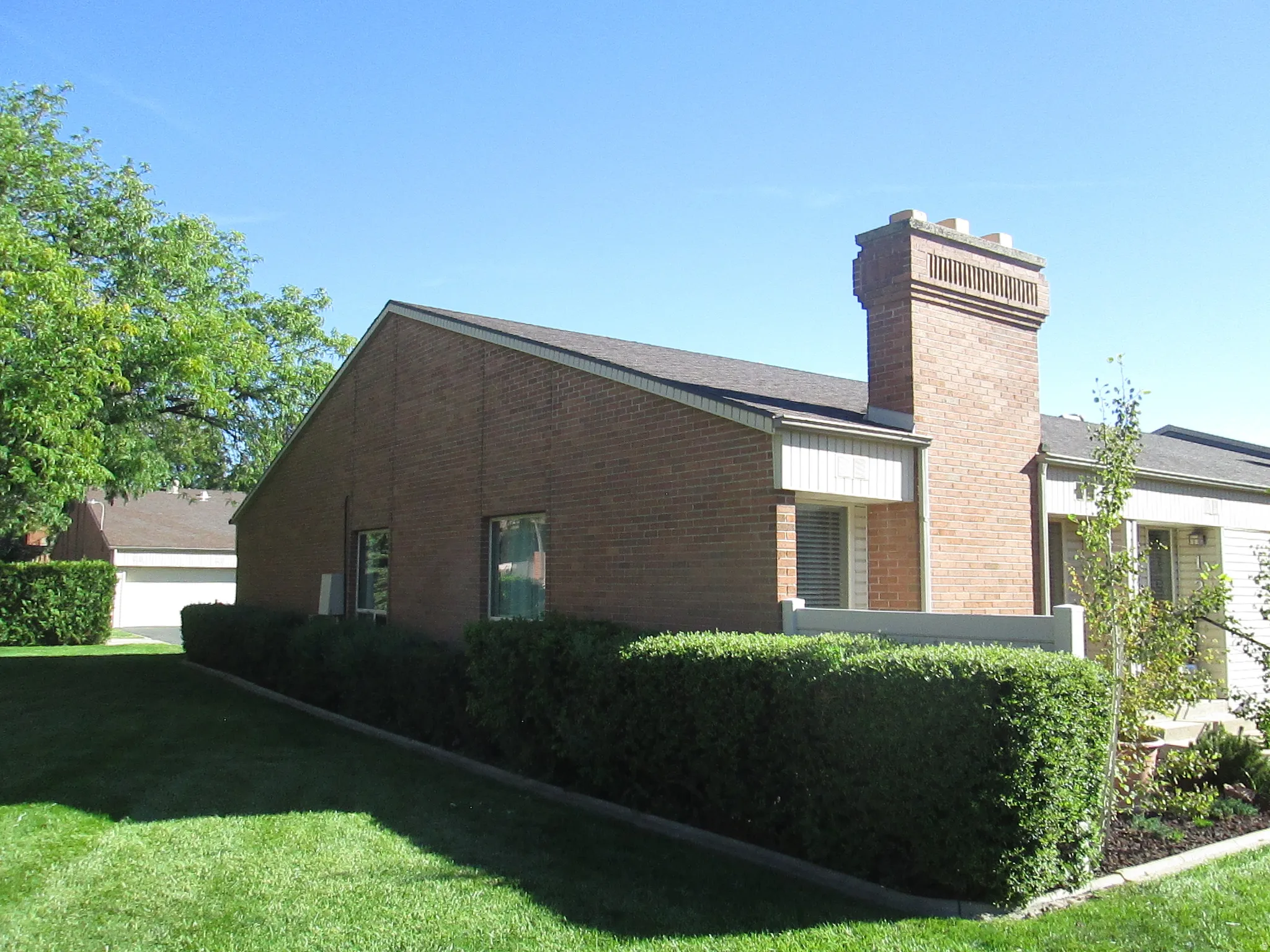 Brick exterior with a prominent brick chimney, gabled roofline, and landscaped shrubbery