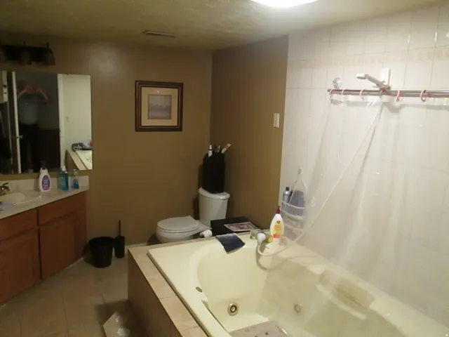 Built-in soaking tub with surrounding tile, single vanity with wood-finish cabinetry, and tiled shower walls