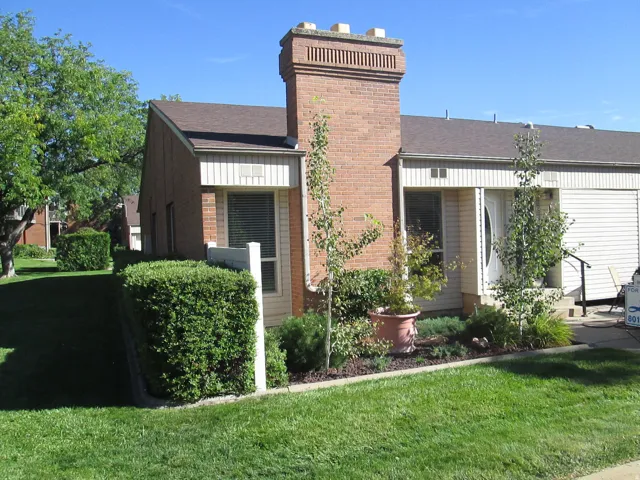 Brick exterior with a prominent brick chimney, pitched shingle roof, manicured lawn, and a landscaped garden bed