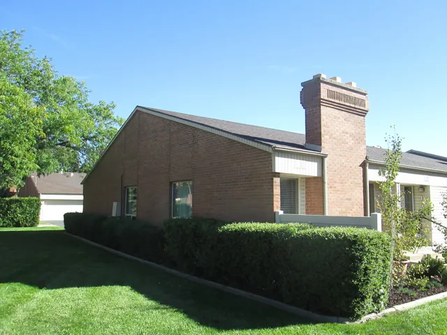 Brick exterior with a prominent brick chimney, gabled roofline, and landscaped shrubbery