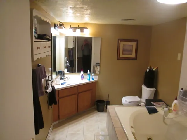 Ceramic tile flooring, built-in shelving, wood-finish vanity with countertop, and a built-in tub