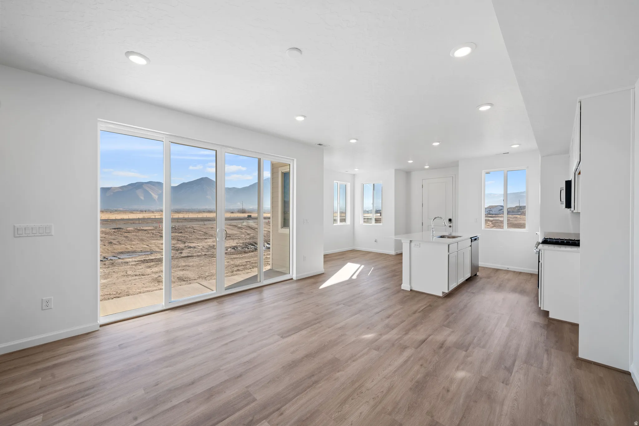 Expansive sliding glass doors, recessed lighting, wood-finish flooring, kitchen island with sink, and white cabinetry