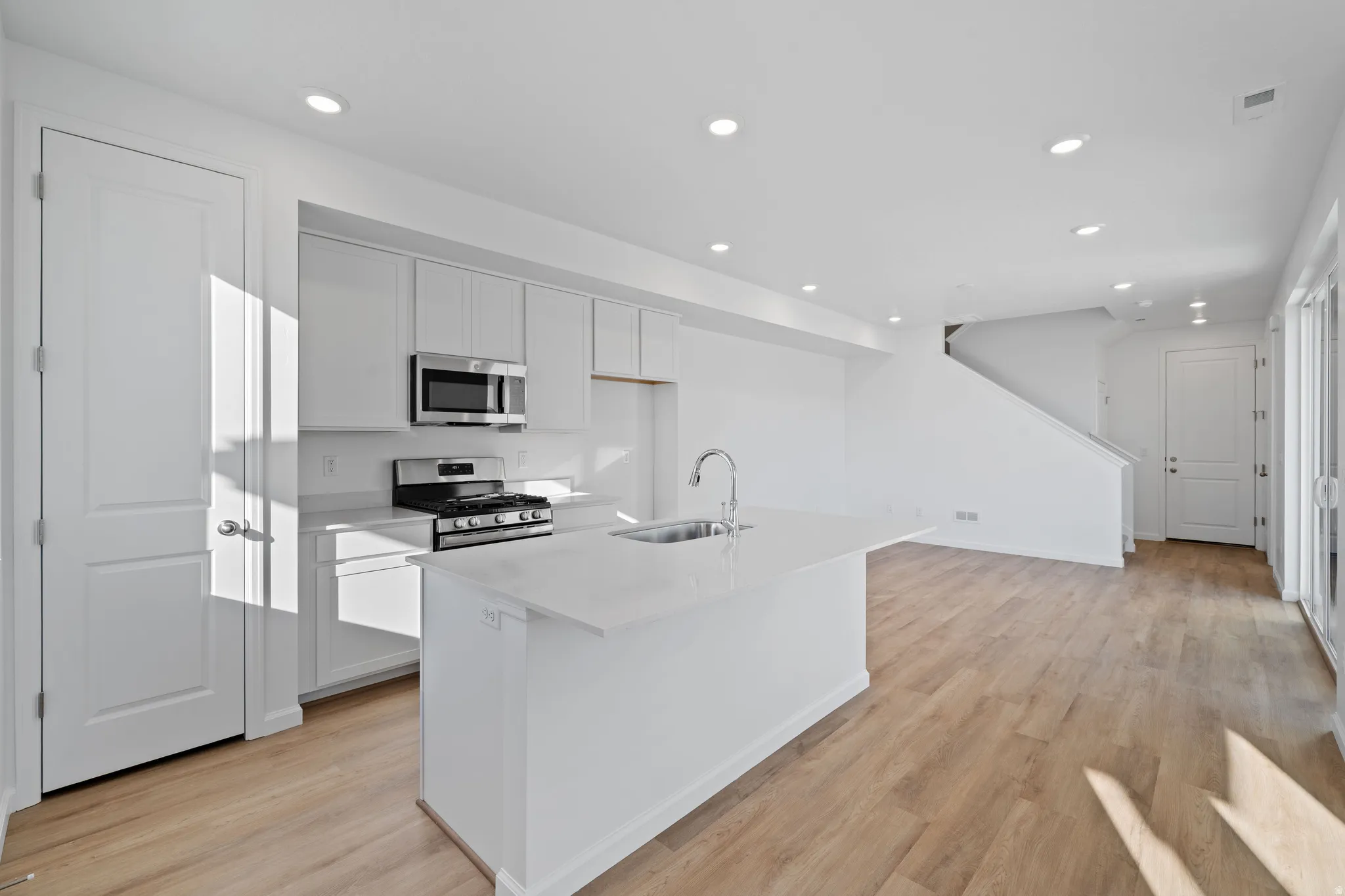 Modern kitchen featuring stainless steel appliances, white cabinetry, a central island with an integrated sink, and wood-finish flooring