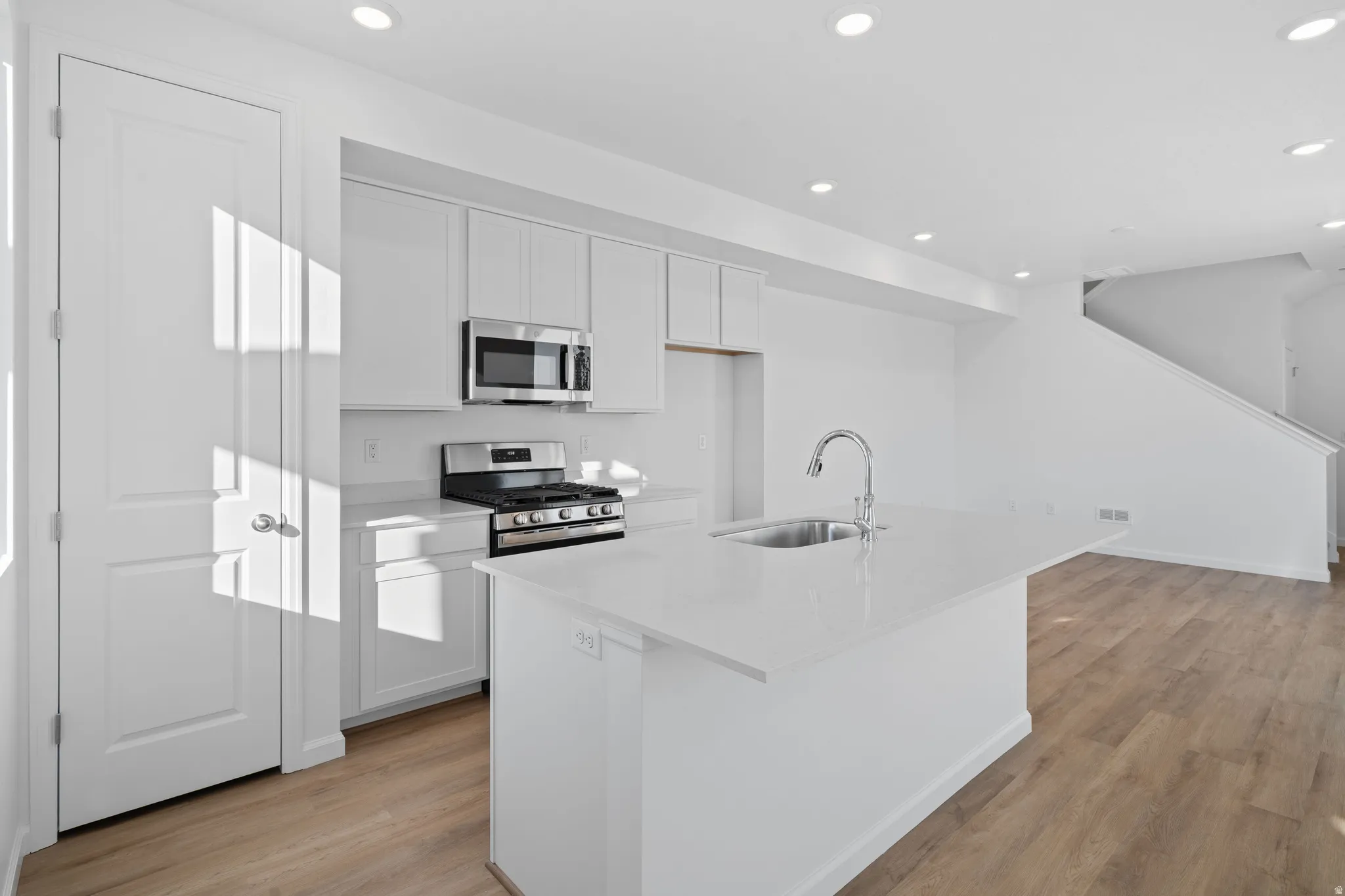 White kitchen featuring a gas range, stainless steel microwave, and wood-finish flooring