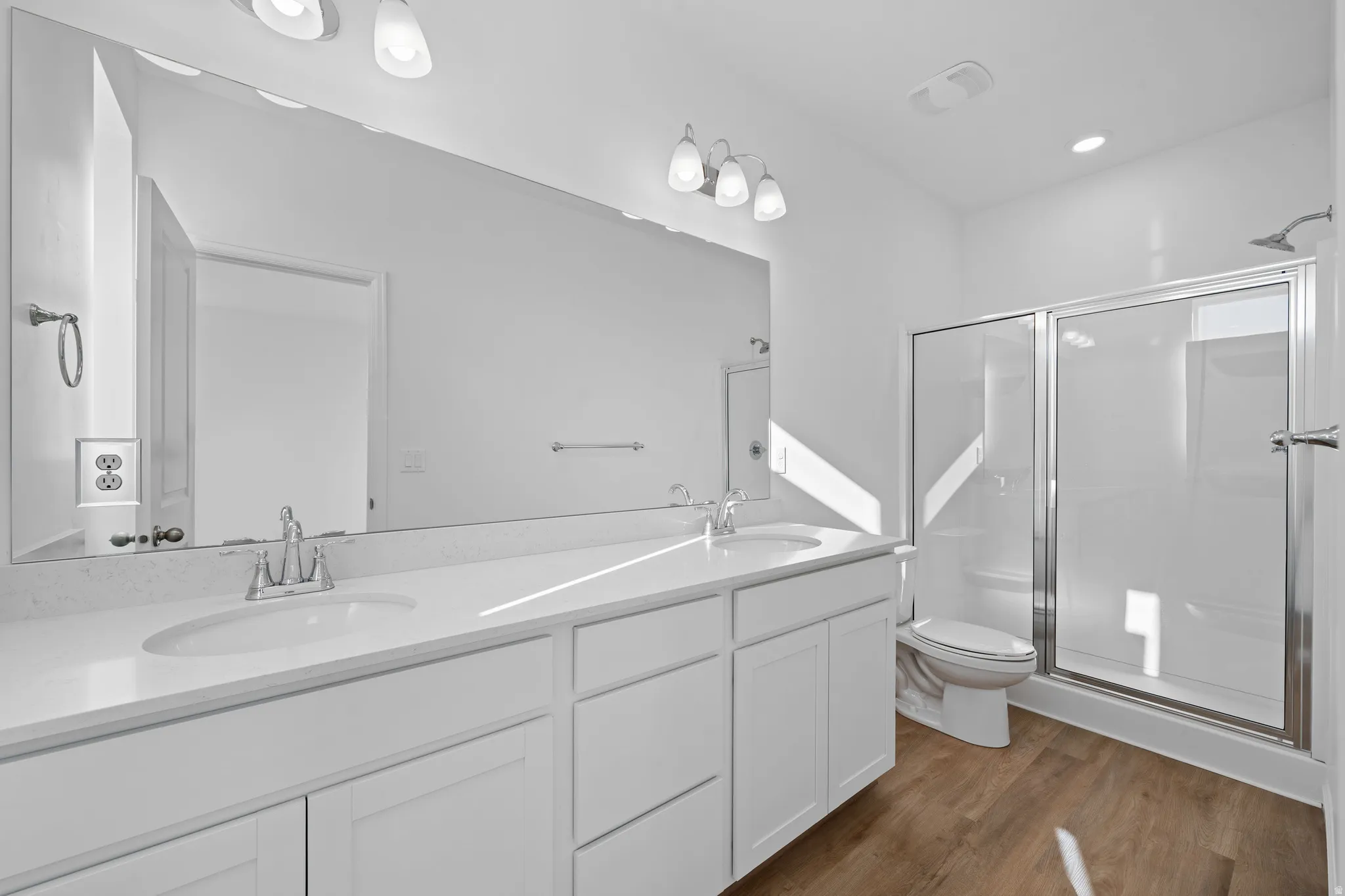 Dual sink vanity with white cabinetry, a large frameless mirror, and a glass-enclosed shower with a sliding door