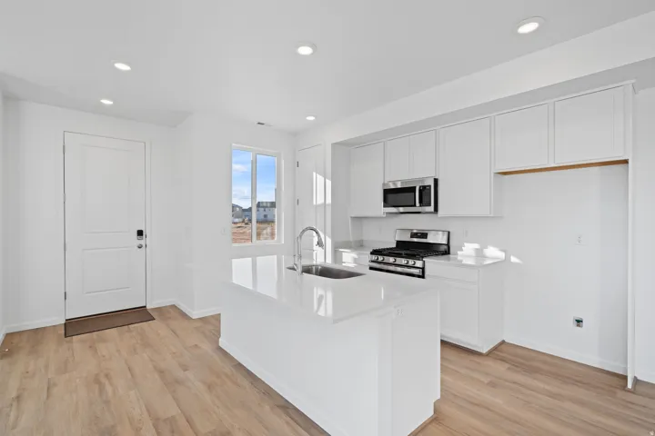 Contemporary kitchen featuring white cabinetry, stainless steel appliances, a center island with sink, recessed lighting, and wood-finish flooring