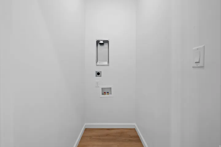 Laundry alcove with a recessed washer hookup, dryer outlet, and wood-finish flooring