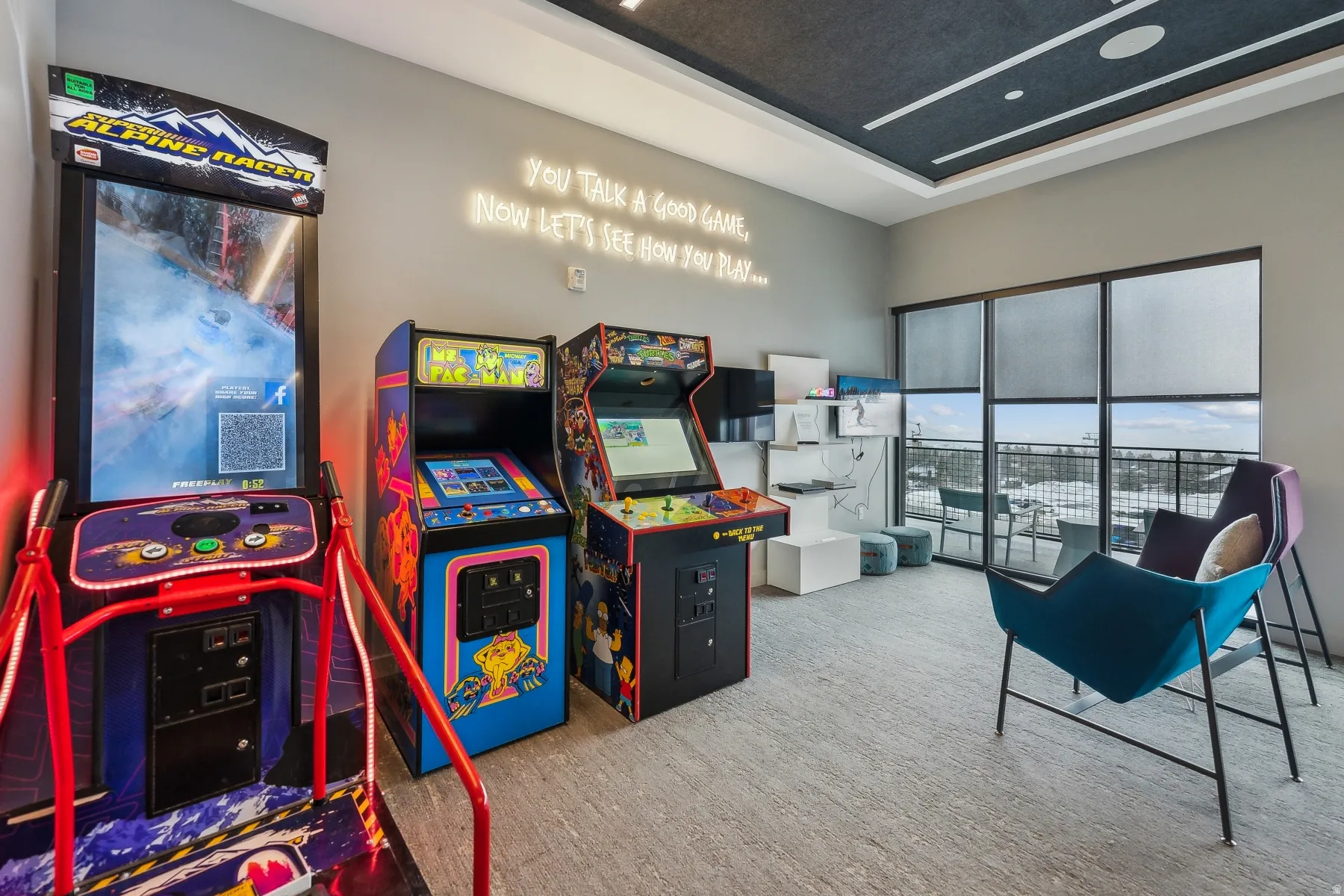 Gaming area featuring multiple arcade machines, a neon wall art installation, and a textured ceiling