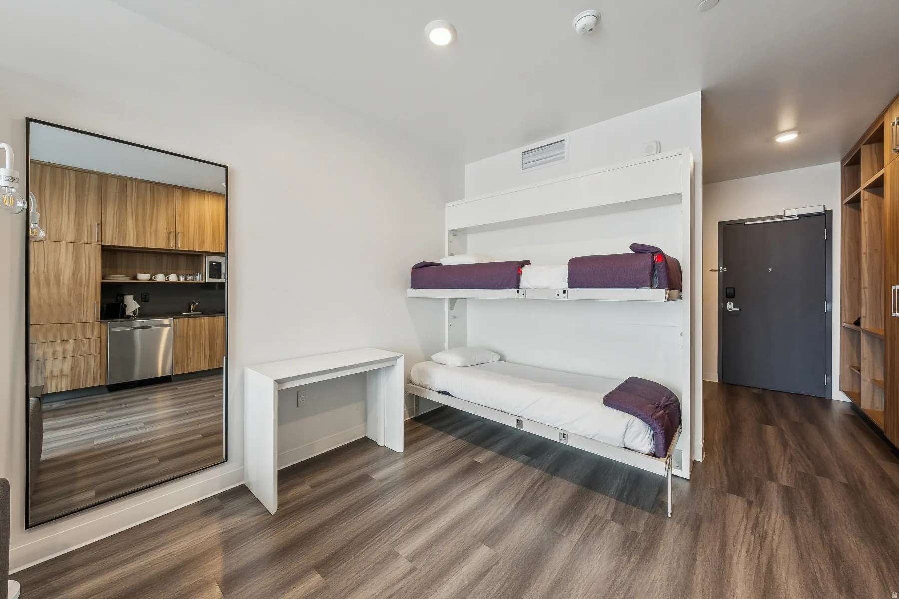 Compact living space featuring wood-finish flooring, a built-in bunk bed system, and a functional kitchenette with stainless steel appliances