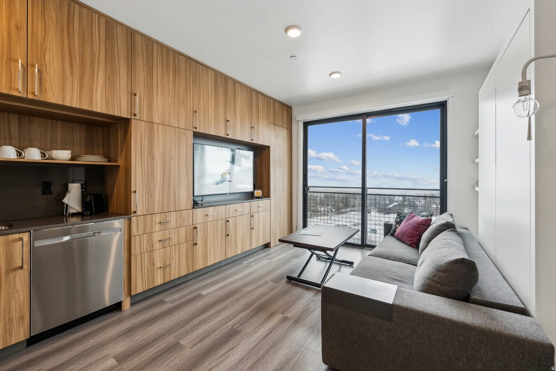 Integrated cabinetry with wood-finish doors, built-in stainless steel dishwasher, and built-in television