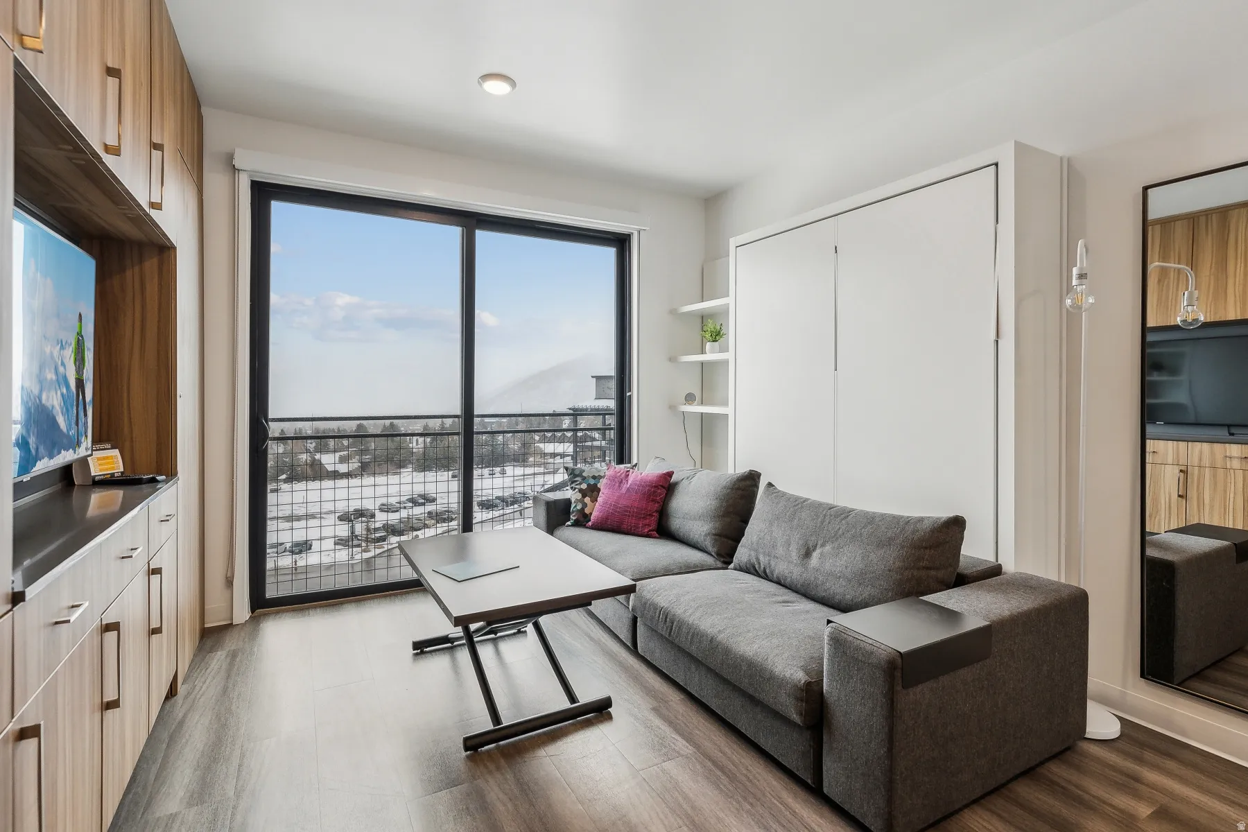 Full-height wood-finish cabinetry, built-in shelving, wall-mounted storage, and a large sliding glass door to a balcony