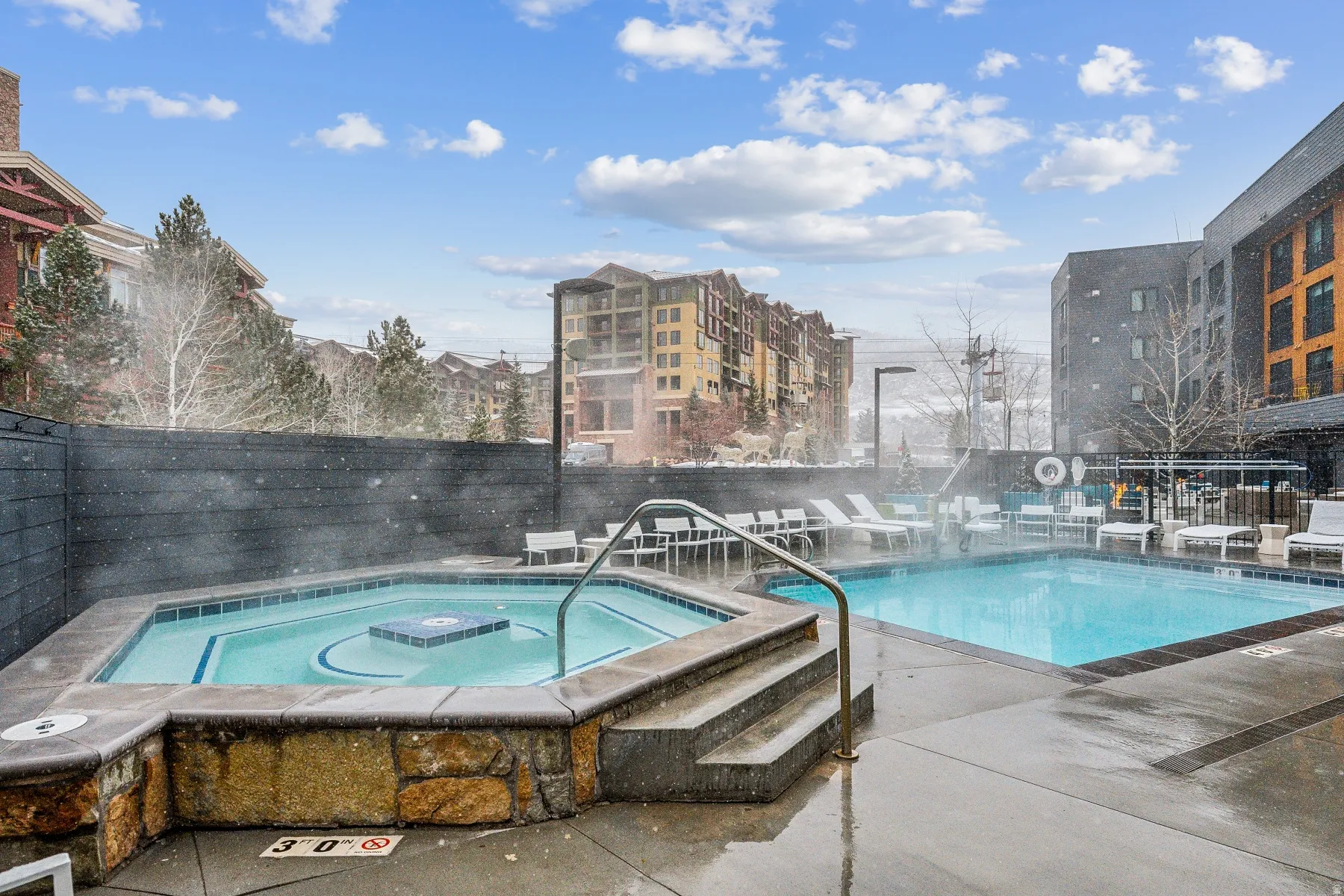 Outdoor swimming pool with integrated spa, surrounded by a stone-clad hot tub and concrete decking