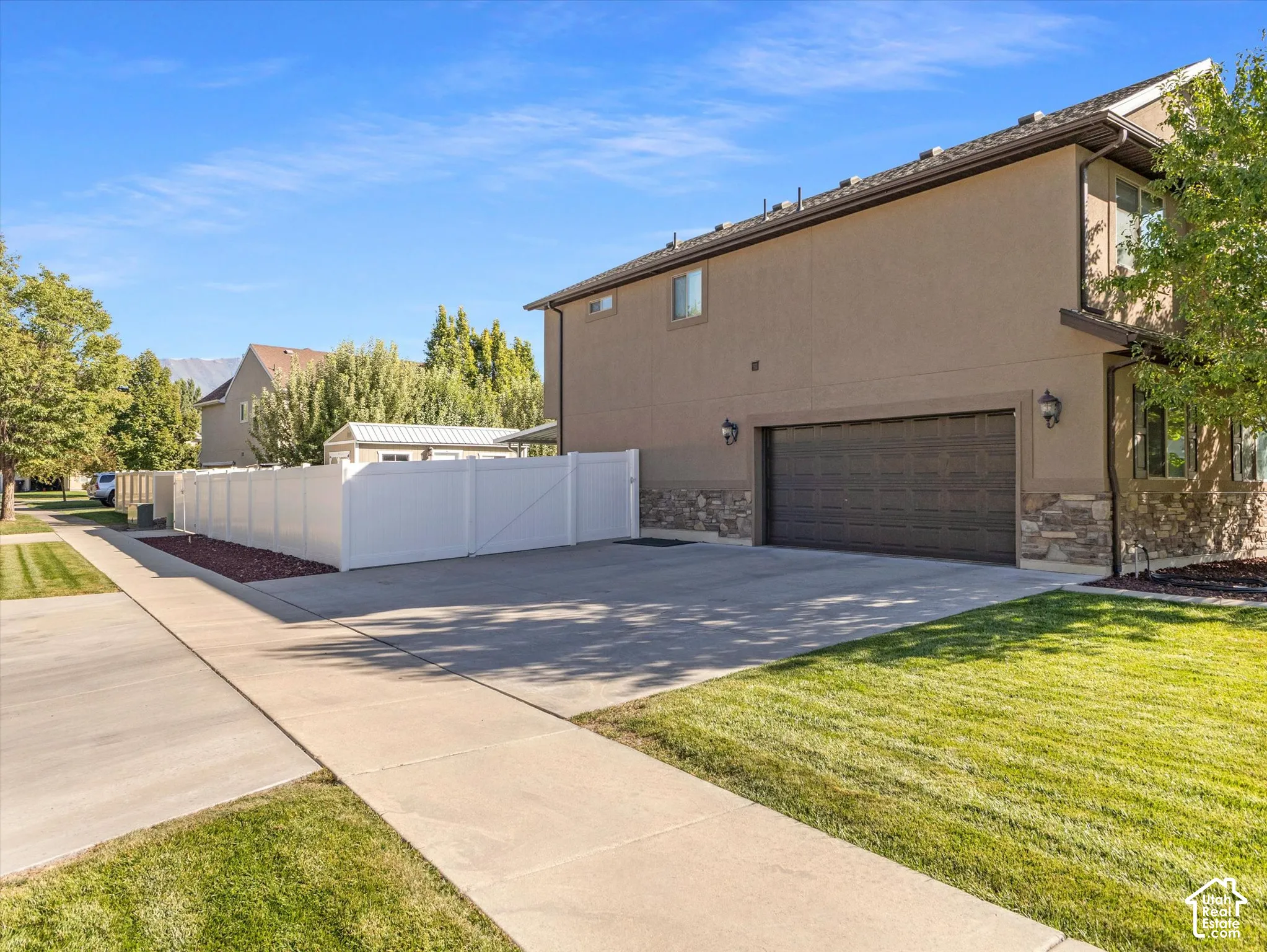 Stucco exterior with stone accenting, attached two-car garage, concrete driveway, and white vinyl fencing