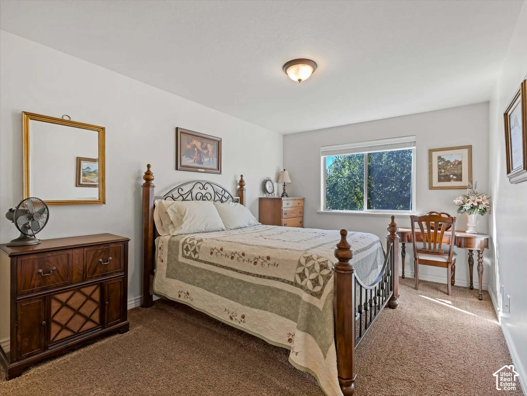 White wall paint, window with exterior foliage, carpeted flooring, and a ceiling-mounted light fixture