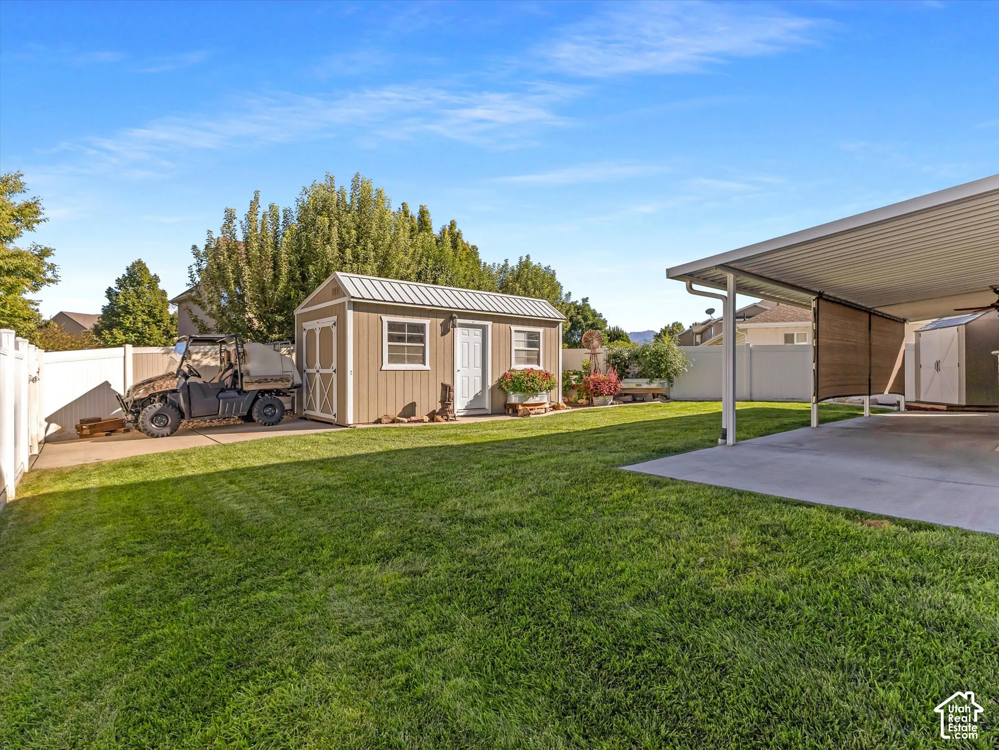 Expansive lawn with a white vinyl fence, a detached storage shed, a covered patio area, and concrete paving
