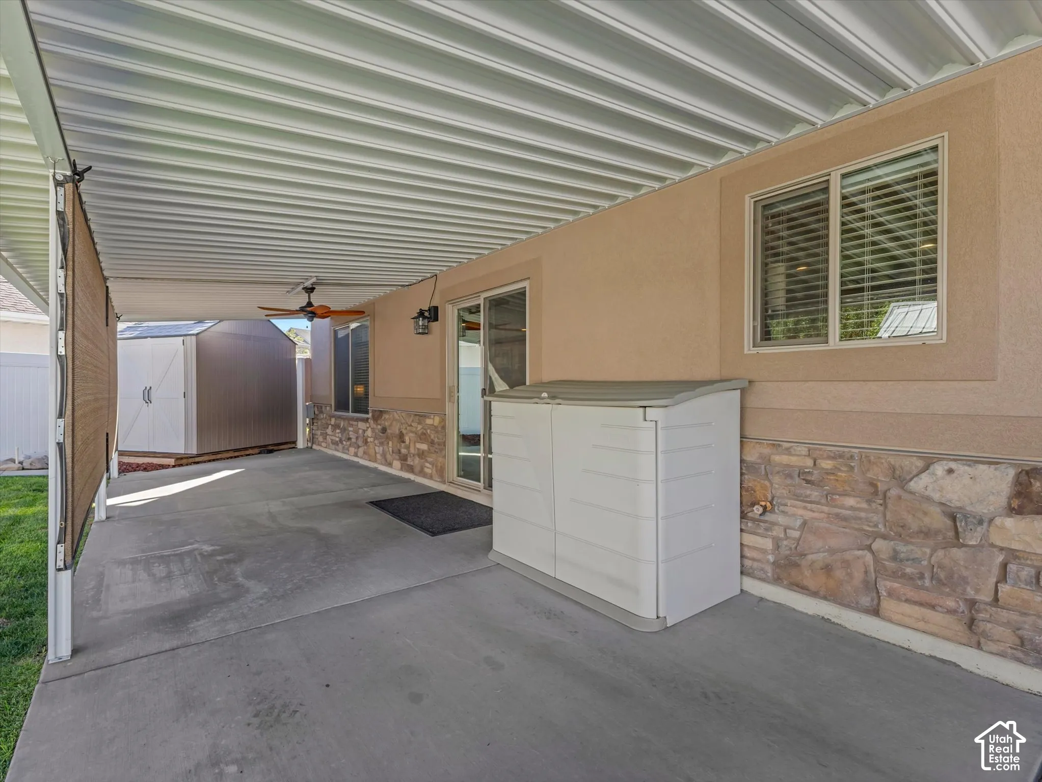 Covered patio with concrete flooring, stone veneer detailing, and ceiling fan