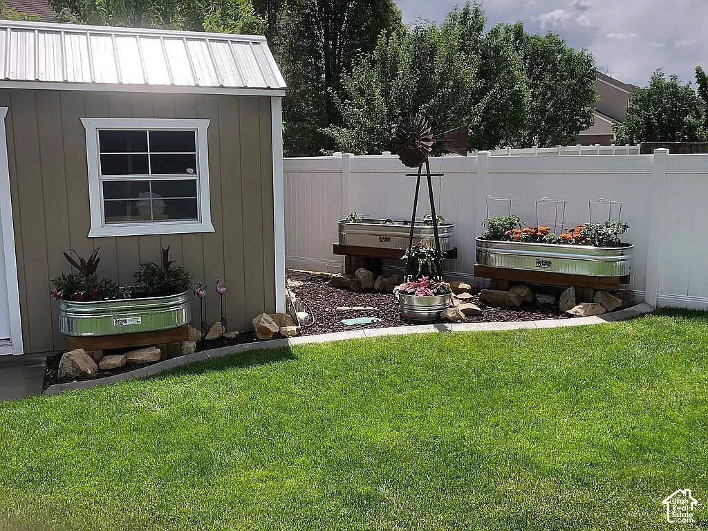 Shed with metal roof, raised garden beds, white privacy fencing, and a grass lawn
