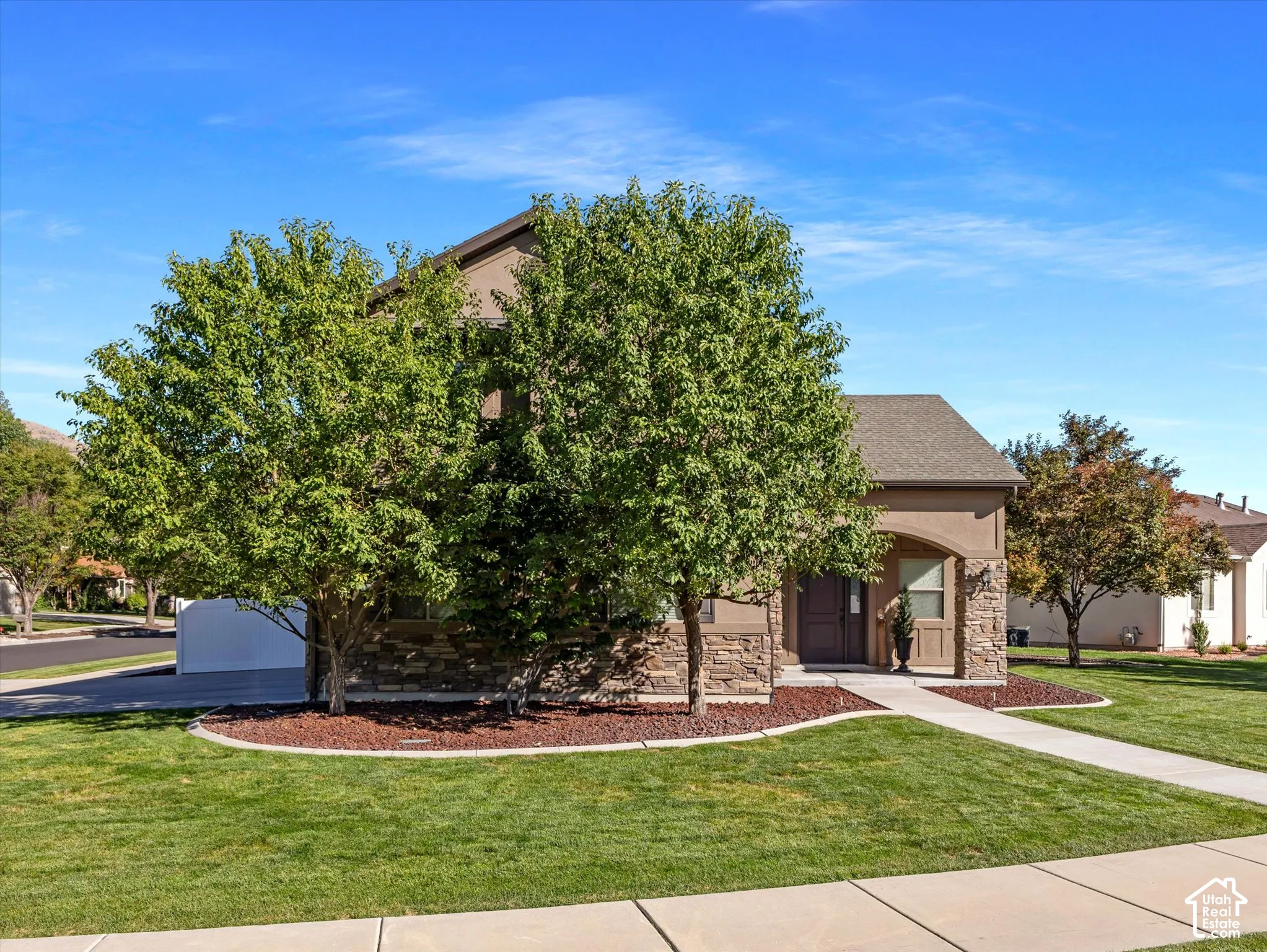 Stucco exterior with stone veneer accents, arched entryway, gabled roof, and concrete pathway