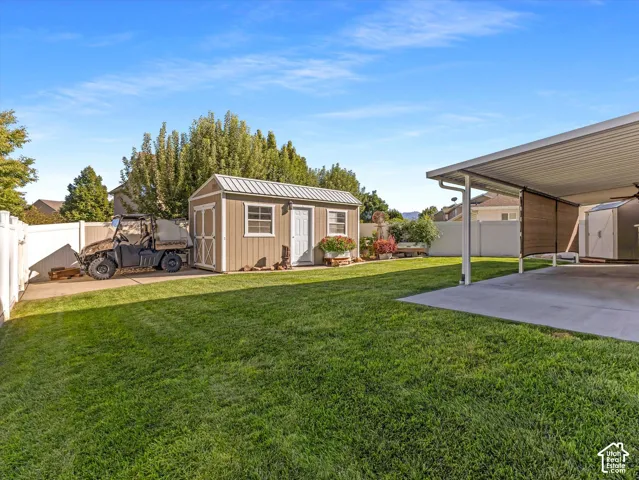 Expansive lawn with a white vinyl fence, a detached storage shed, a covered patio area, and concrete paving