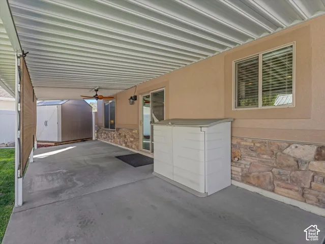 Covered patio with concrete flooring, stone veneer detailing, and ceiling fan